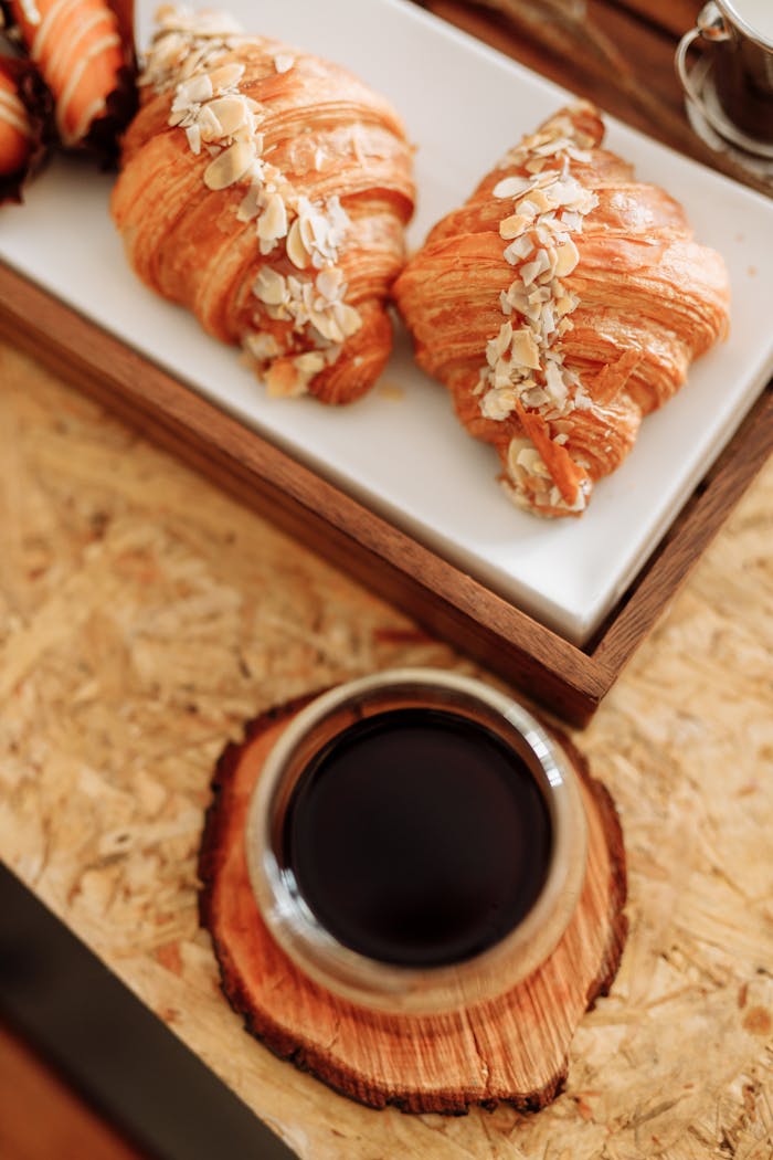 services-04 Fresh almond croissants served with coffee on a rustic wooden table.